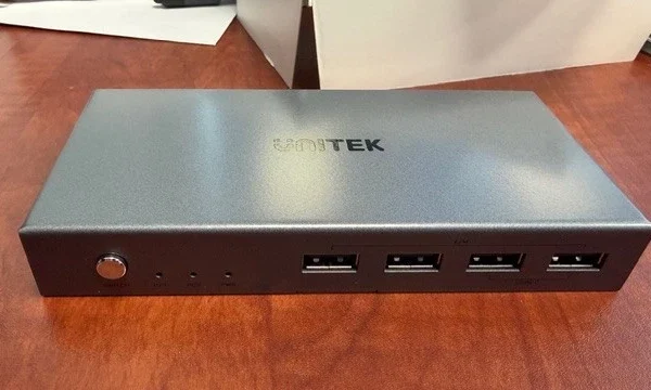 Ảnh thực tế Bộ KVM HDMI Unitek V307A đặt trên bàn làm việc tại văn phòng TranNamPC — logo UNITEK in nổi trên mặt đỉnh kim loại nhám, nút SWITCH và 4 cổng USB-A mặt trước